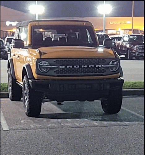 A Yellow Ford Bronco Is Parked In A Parking Lot At Night GIF