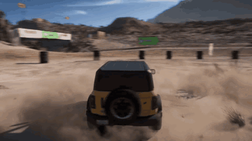 A Yellow Jeep Is Driving Down A Dirt Road With A Green Sign In The Background GIF
