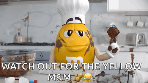 A Yellow M&m Wearing A Chef Hat Is Holding A Brownie GIF