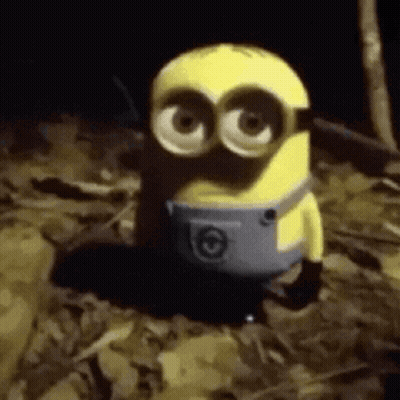 A Yellow Minion Is Standing In A Pile Of Leaves . GIF