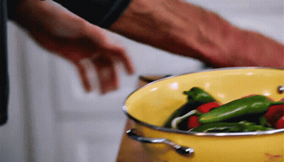 A Yellow Pot Filled With Green And Red Peppers Is Being Stirred By A Person GIF