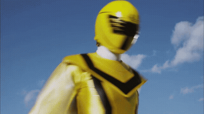 A Yellow Power Ranger Stands In Front Of A Blue Sky With Clouds GIF