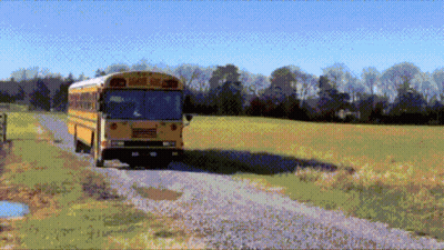 A Yellow School Bus Driving Down A Dirt Road GIF