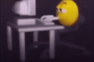 A Yellow Smiley Face Is Sitting In Front Of A Computer Monitor . GIF