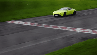 A Yellow Sports Car Is Driving Down A Road With Grass In The Background GIF