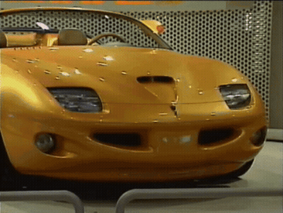 A Yellow Sports Car Is Parked In Front Of A Wall That Has Holes In It GIF
