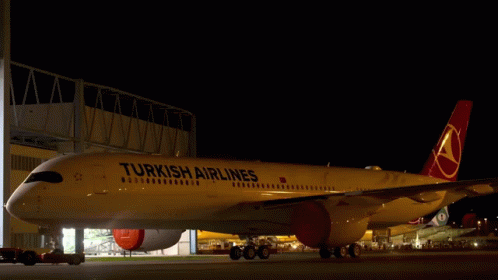 A Yellow Turkish Airlines Plane Is Parked In A Hangar At Night GIF