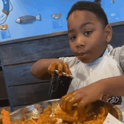 A Young Boy Eating Food With A Cup That Says Crab On The Front GIF
