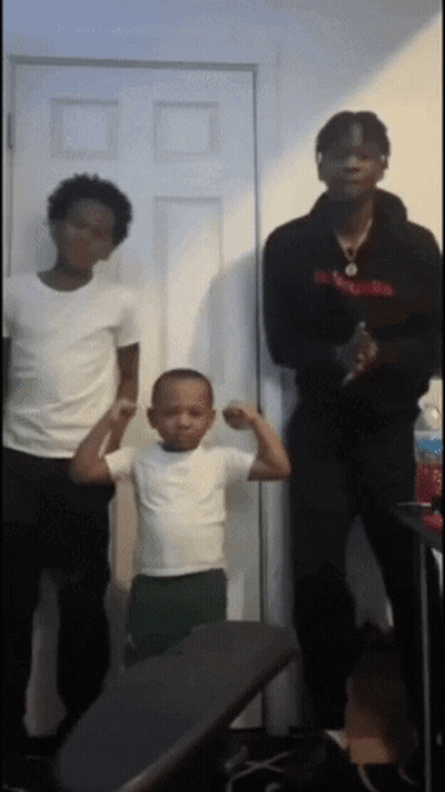A Young Boy Flexes His Muscles While Standing Next To Two Men GIF
