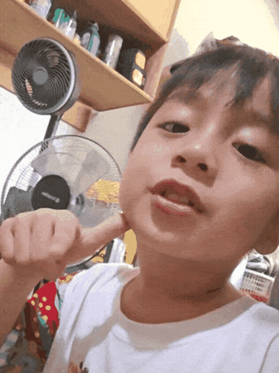 A Young Boy Holds His Fist Up In Front Of A Fan GIF