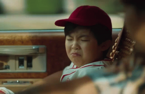 A Young Boy In A Baseball Cap Is Sitting In The Back Seat Of A Car Making A Funny Face . GIF