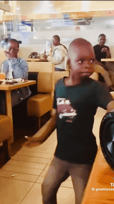 A Young Boy In A Black Shirt With A Car On It Is Dancing In A Restaurant GIF