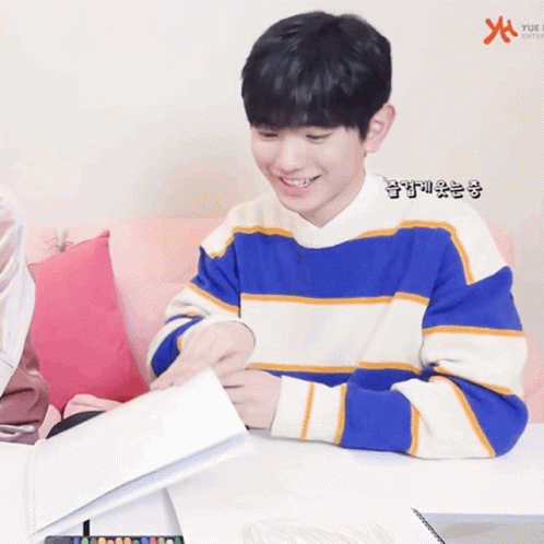 A Young Boy In A Blue And White Striped Sweater Is Sitting At A Table Holding A Piece Of Paper GIF