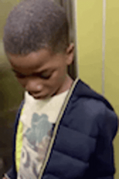 A Young Boy In A Blue Jacket Is Standing In An Elevator Looking Down . GIF