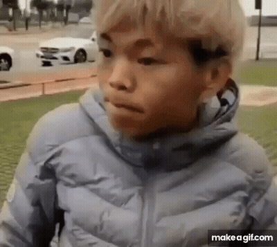 A Young Boy In A Blue Jacket Is Standing In Front Of A White Car And Making A Funny Face . GIF