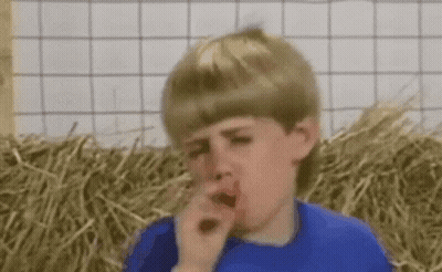 A Young Boy In A Blue Shirt Is Coughing In Front Of Hay Bales . GIF