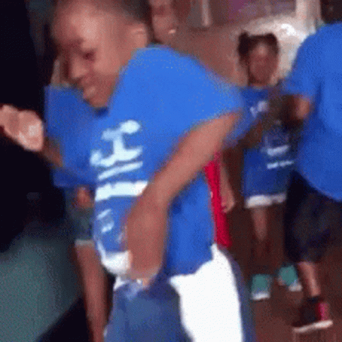 A Young Boy In A Blue Shirt Is Dancing In A Crowd Of People . GIF