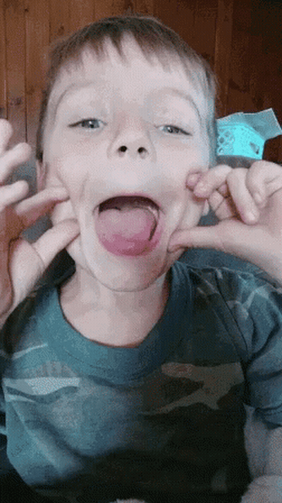 A Young Boy In A Blue Shirt Is Making A Funny Face With His Tongue Out GIF