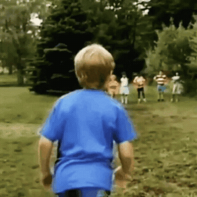 A Young Boy In A Blue Shirt Is Running Towards A Group Of Children In A Park . GIF