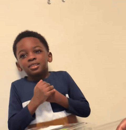 A Young Boy In A Blue Shirt Is Sitting At A Table GIF