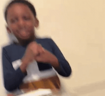 A Young Boy In A Blue Shirt Is Sitting At A Table With A Bottle Of Beer . GIF