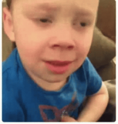 A Young Boy In A Blue Shirt Is Sitting On A Couch And Making A Funny Face . GIF