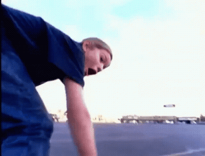 A Young Boy In A Blue Shirt Is Standing In A Parking Lot GIF