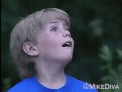 A Young Boy In A Blue Shirt Looks Up At The Sky GIF