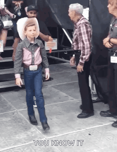 A Young Boy In A Cowboy Outfit Is Walking Towards A Man In A Plaid Shirt . GIF