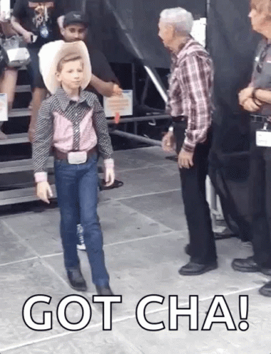 A Young Boy In A Cowboy Outfit Is Walking Towards A Man With The Words Got Cha Written On The Ground GIF