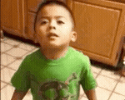 A Young Boy In A Green Shirt Is Standing On A Tiled Floor . GIF