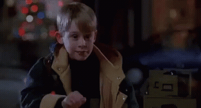 A Young Boy In A Jacket Is Standing In Front Of A Christmas Tree And A Car . GIF