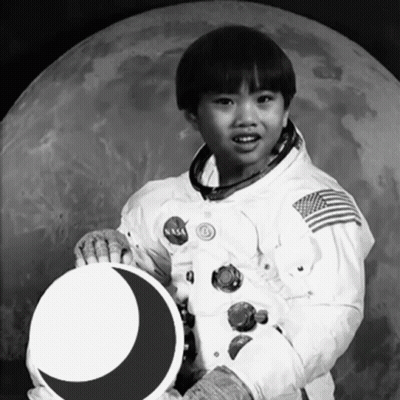 A Young Boy In A Nasa Space Suit Is Holding A Crescent Moon GIF