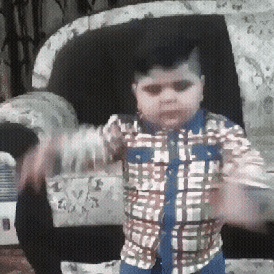 A Young Boy In A Plaid Shirt Is Standing In Front Of A Couch . GIF