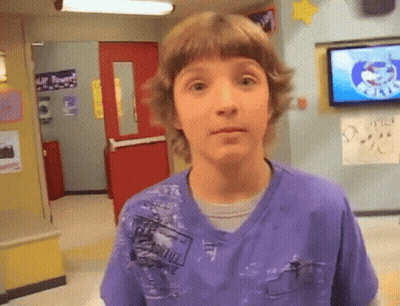 A Young Boy In A Purple Shirt Is Standing In Front Of A Tv In A Hallway GIF