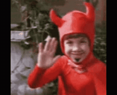 A Young Boy In A Red Devil Costume Is Waving . GIF