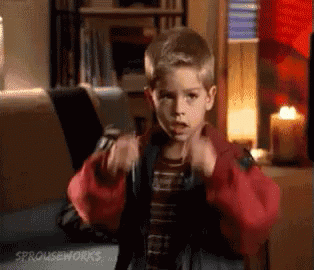 A Young Boy In A Red Jacket Is Sitting In Front Of A Laptop Computer In A Living Room . GIF