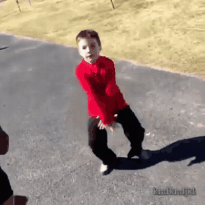 A Young Boy In A Red Shirt Is Dancing On A Sidewalk GIF