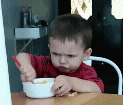 A Young Boy In A Red Shirt Is Eating Cereal With A Spoon GIF