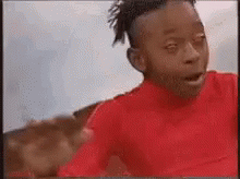 A Young Boy In A Red Shirt Is Making A Funny Face While Looking At The Camera . GIF