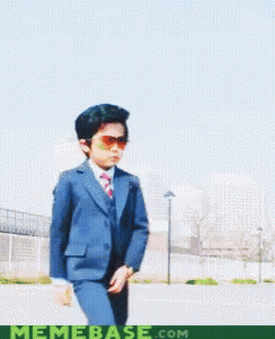 A Young Boy In A Suit And Tie Holds A Pair Of Glasses In Front Of A Memebase.com Logo GIF