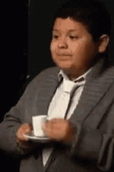 A Young Boy In A Suit And Tie Is Drinking A Cup Of Coffee . GIF