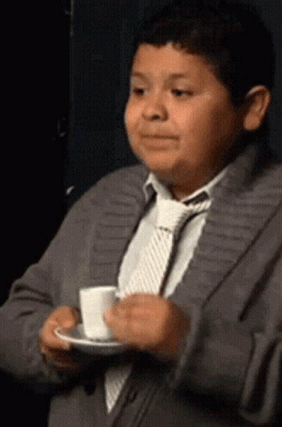 A Young Boy In A Suit And Tie Is Holding A Cup Of Coffee On A Saucer . GIF