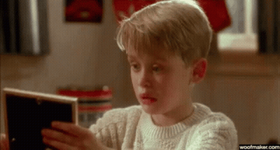 A Young Boy In A Sweater Is Looking At A Picture In A Frame . GIF