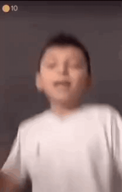 A Young Boy In A White Shirt Is Making A Funny Face And Dancing . GIF