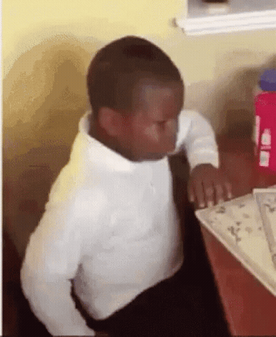 A Young Boy In A White Shirt Is Sitting At A Table With A Book . GIF