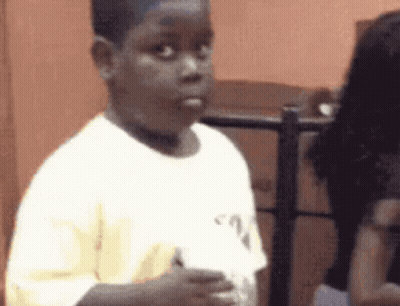 A Young Boy In A White Shirt Is Standing In Front Of A Woman . GIF