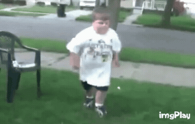 A Young Boy In A White Shirt Is Walking On A Sidewalk . GIF