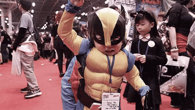 A Young Boy In A Wolverine Costume Is Standing In A Crowd . GIF