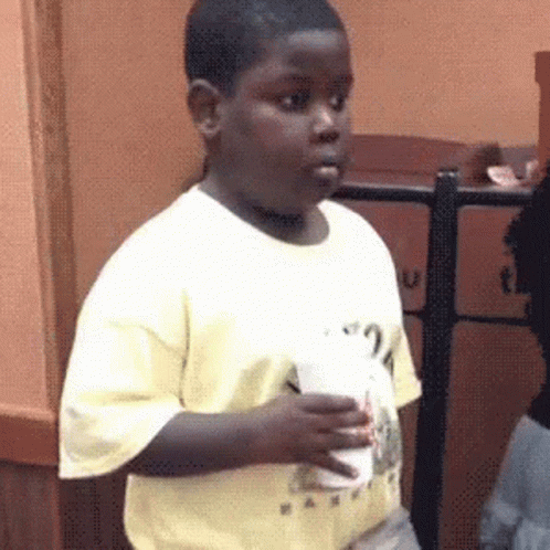 A Young Boy In A Yellow Shirt Is Holding A Cup Of Coffee . GIF